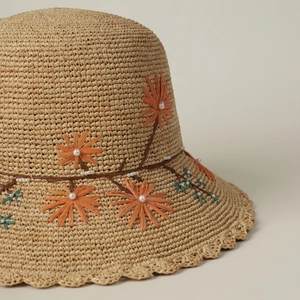 Detailed close-up of orange floral embroidery and white pearls on woven raffia hat