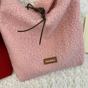 Detalle de bolso de felpa rosa con etiqueta de cuero marrón y cierre de cordón ajustable
