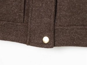 Detailed close-up of dark brown wool jacket hem with precision stitching and gold button