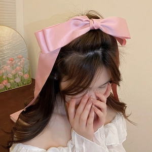 Pink satin bow hair clip with long ribbons worn by model in a natural setting