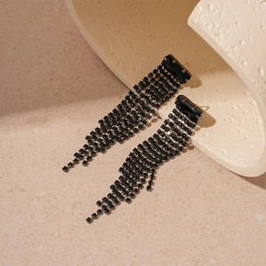 Detail of long black tassel earrings with geometric zircon studs and crystal chains