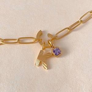Collana in acciaio al titanio dorato con lettera K incisa e pendente in cristallo viola