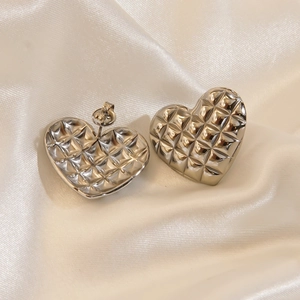 Silver stainless steel heart earrings with quilted texture on white silk fabric background