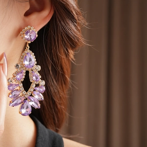 Close-up of elegant gold drop earrings with purple crystals and sparkling rhinestones