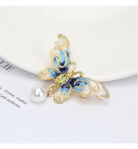 Detail view of gold butterfly brooch with blue enamel wings, zircons and pearl drop