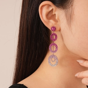 Detailed view of layered geometric hoop earrings with pink rhinestones on a female model