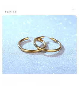 Detail of high-polished gold hollow hoop earrings made of stainless steel on blue background