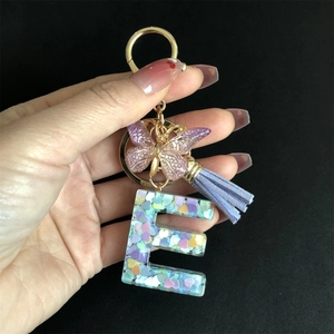 Detail of purple resin letter E keychain with gold butterfly and heart sequins