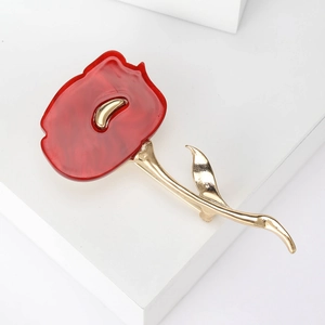 Detailed macro shot of red flower brooch with golden leaves on white geometric block