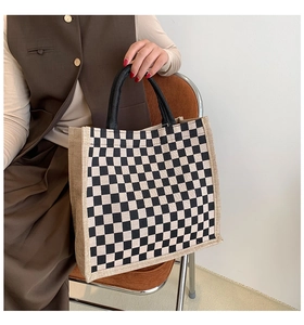 Detail of checkered canvas tote bag with black handles held by model in natural light