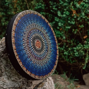 Handcrafted Shamanic drum with mosaic mandala pattern leaning on a forest rock
