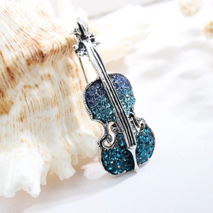 Elegant violin brooch featuring blue gradient rhinestones on a white textured background