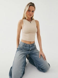 Detail of beige sleeveless knit crop top paired with blue jeans in a studio shot