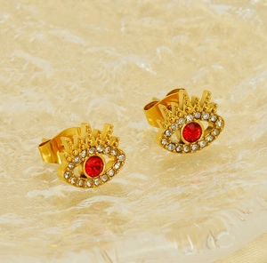 Detail of gold-plated evil eye stud earrings with red zircon and white crystal accents
