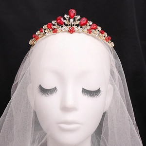 Elegant gold bridal crown with red teardrop rhinestones and a white lace veil on dark background