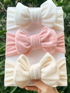Three-pack corduroy bow headbands for babies in white, pink, and beige on a card