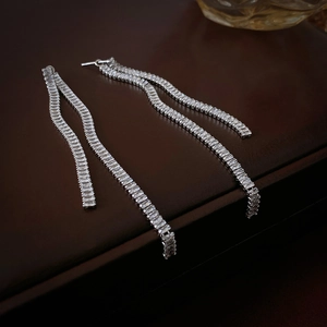 Detailed view of silver tassel earrings with rectangular cubic zirconia on brown leather