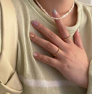 Close-up of a white pearl necklace and two gold twisted knot rings on a model