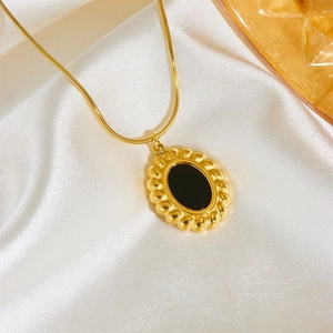 Vintage gold oval pendant necklace with black enamel inlay on a soft white silk background