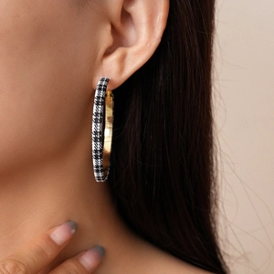 Close-up detail of oversized houndstooth fabric hoop earring with golden metal accents