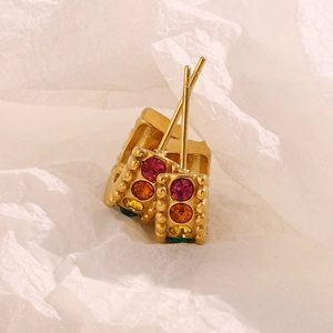 Macro detail of 18K gold plated C-shaped earrings with colorful zircon stones on white paper