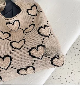 Détail de la texture d'un sac cabas en maille beige avec motifs de cœurs noirs poilus