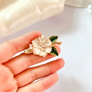 Detail of white enamel poppy brooch with green leaves and pearl accents on gold base
