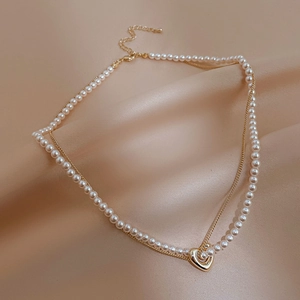 Detail view of double-layer necklace with small white pearls and gold heart pendant on silk