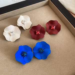 Close-up of matte floral earrings in white, red, and blue with central square crystals