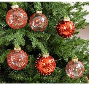 Close-up of red glitter Christmas ornaments with gold patterns on a green tree branch