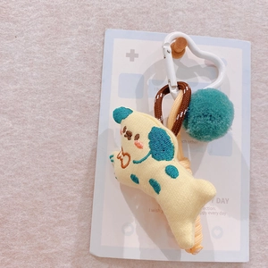 Detail of yellow plush animal keychain with green pompom and woven strap on pink felt