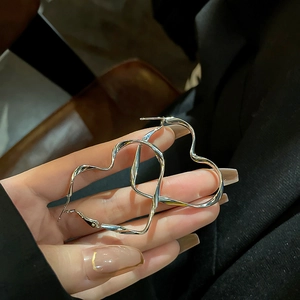 Polished silver heart-shaped hoop earrings with a twisted design held in hand