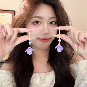 Detail of purple resin flower earrings with white pearl tassels held by a model