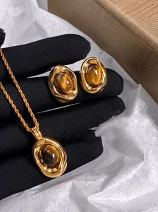 Detailed view of oval tiger eye stone necklace and earring set held in black gloves