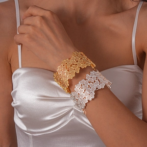 Détail de bracelets manchettes larges en or et argent avec des motifs de dentelle florale évidés