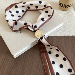 Polka dot silk scarf with golden ring buckle on vintage book and dark wood background