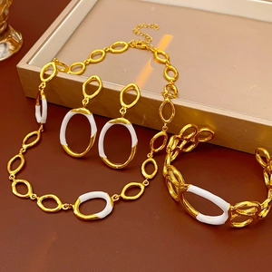Detailed view of luxury gold jewelry set with white enamel links on a beige display tray