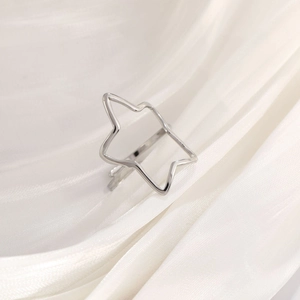 Macro view of a silver star-shaped open ring on white silk, showing polished metal texture