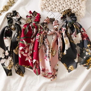 Flat lay of satin ponytail scrunchies with floral and leopard prints on a white fabric