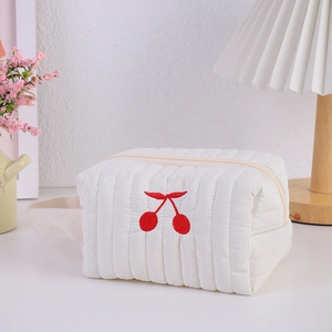 Close-up of cute cherry embroidery on a white quilted vanity bag with top handle