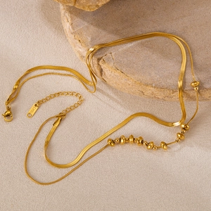 Detail of layered gold stainless steel snake chain and beaded necklace with S.STEEL stamp