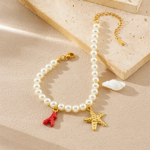 Vue détaillée du bracelet de perles avec étoile de mer dorée, corail et breloques coquillages