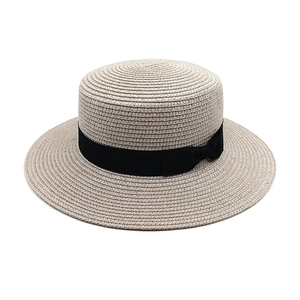 Detail of a beige straw boater hat featuring a wide black ribbon and a delicate bow knot