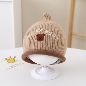 Détail du bonnet tricoté pour bébé avec broderie Lucky Baby et écusson d'ourson