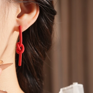 Close-up of stylish red knotted earrings with matte finish worn by model in soft light