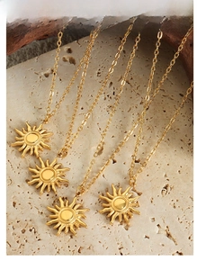 Detail of 18K gold plated sun pendant necklaces on a natural beige stone base