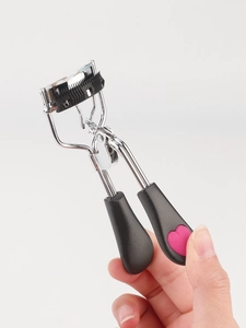 Detail of silver eyelash curler with built-in black comb and pink heart grip design