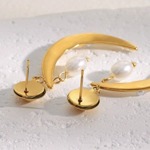 Detail of 18K gold horn earrings featuring white pearl drops on a textured surface