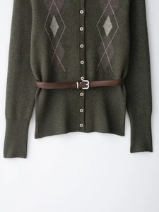 Détail du cardigan en maille losanges vert foncé avec boutons et ceinture en cuir marron