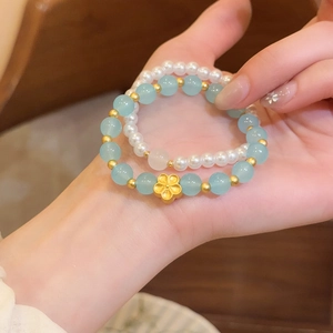 Vista detallada de una pulsera de piedra natural azul claro con flor de oro y anillo de perlas